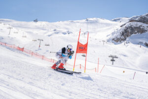 Ein Skifahrer rast die Piste hinunter, an einem orangenen Tor vorbei.